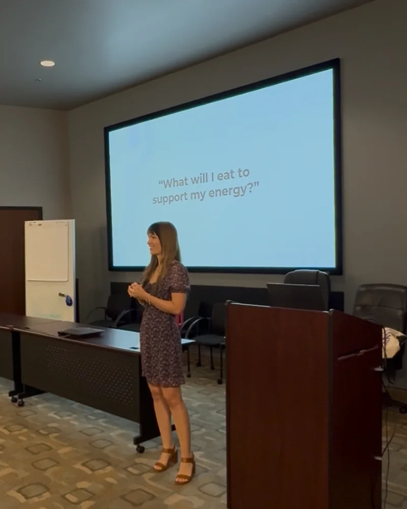 Abigail Parker presenting a corporate session, a slide reading What will I eat to support my energy behind her