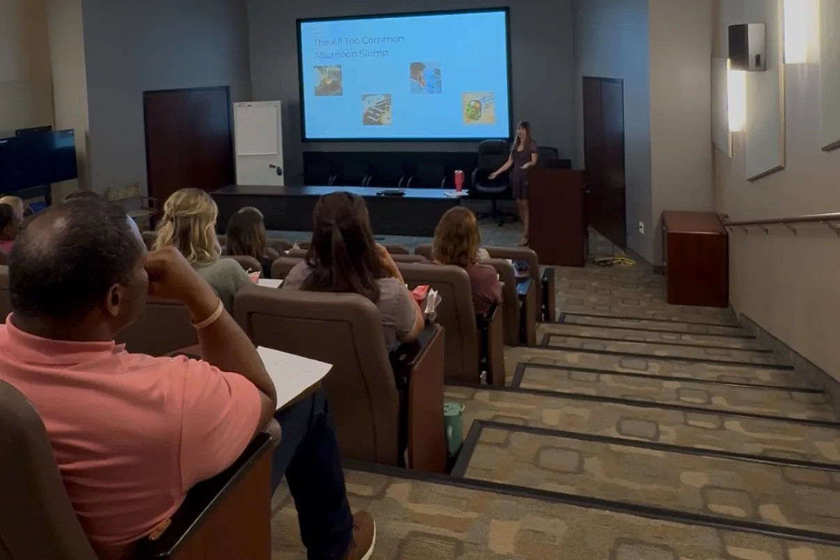 A full room of employees at a real Nourished Revival High Energy Workdays session, an afternoon-slump talk on screen